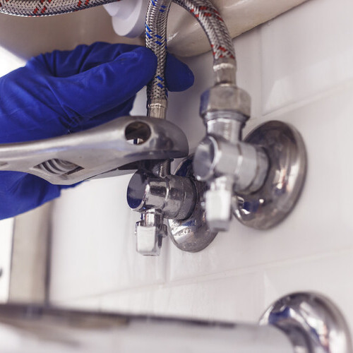 Plumber turns nut on angle valve under wash basin using spreading wrench