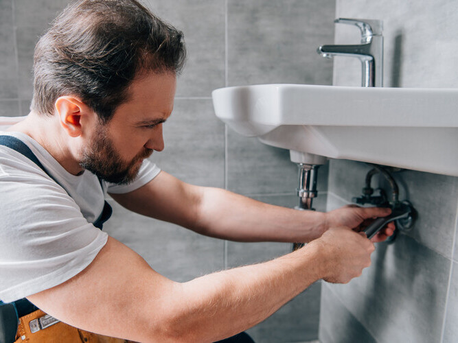 adult male plumber in working overall fixing sink in bathroom