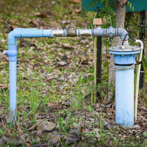 Groundwater well with pvc pipe and system electric deep well submersible pump water on green meadow